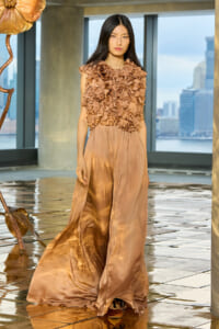 Model wearing a champagne-colored satin gown with a heavily ruffled bodice on a runway