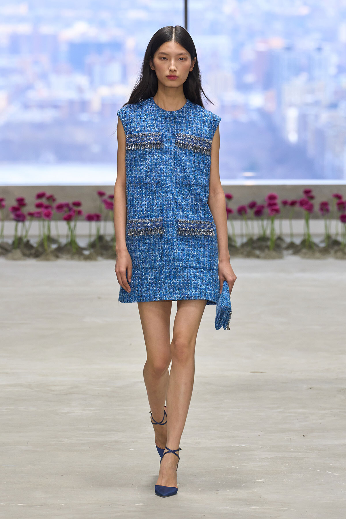 Model walking the runway in a cobalt-blue tweed sleeveless mini dress with fringe-pocket embellishments and a matching blue clutch.