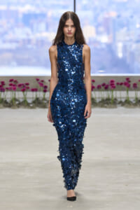 Female model walks the runway in a sleeveless navy blue sequined jumpsuit.