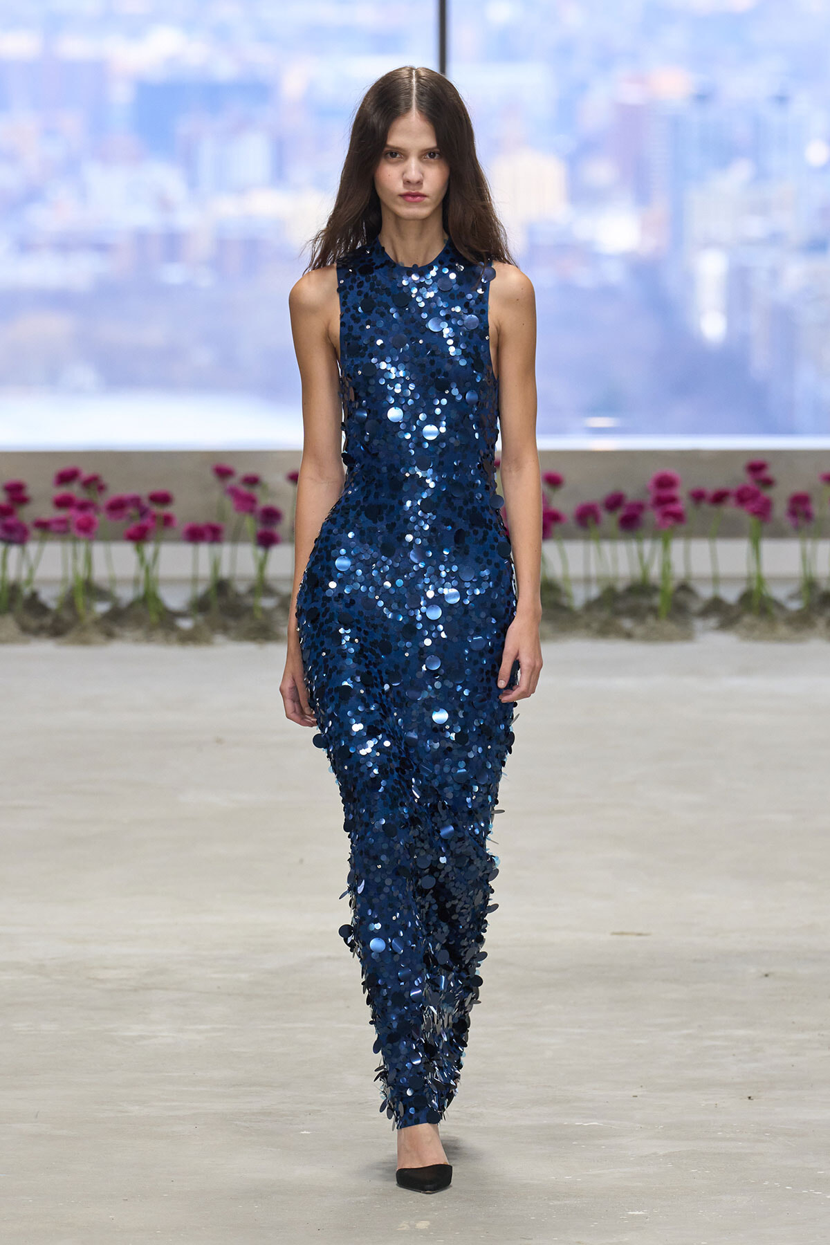 Female model walks the runway in a sleeveless navy blue sequined jumpsuit.
