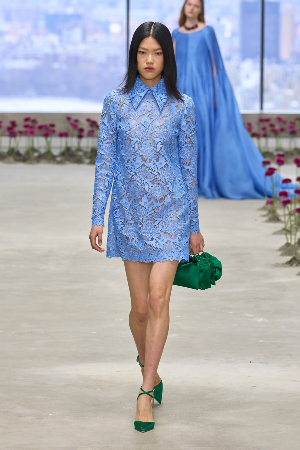 Model walks the runway in a light-blue lace dress with a pointed collar, green heels, and a matching green handbag.