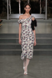 Model walks a floral off-shoulder midi dress with a puffed sleeve, on a runway at night.