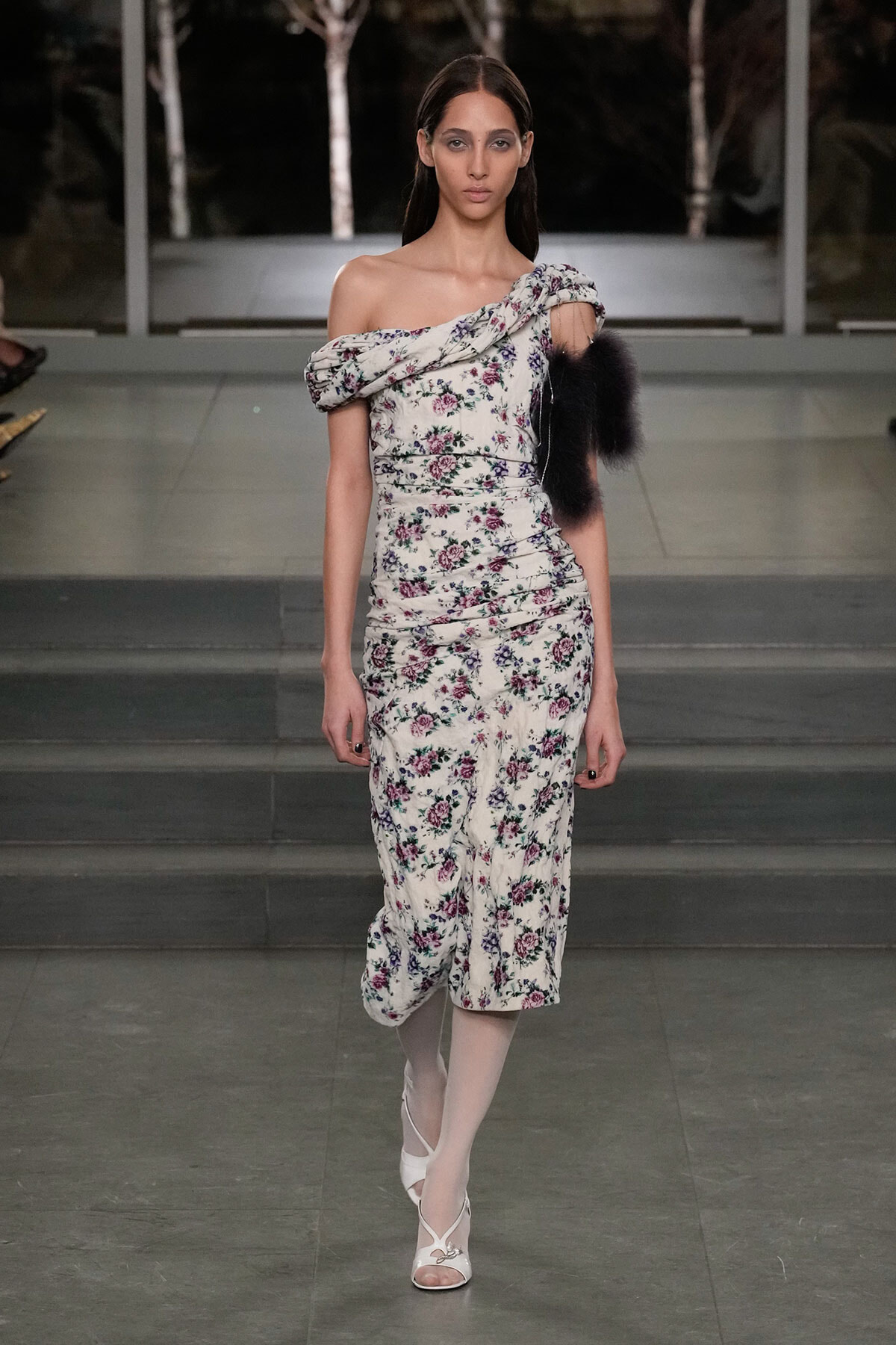 Model walks a floral off-shoulder midi dress with a puffed sleeve, on a runway at night.