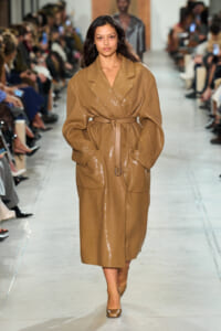 Model walking the runway in a knee-length camel sequin wrap coat with a belt, paired with matching shoes.