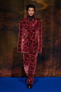 Male model walking a runway in a burgundy velvet floral-pattern suit, double-breasted blazer and matching pants