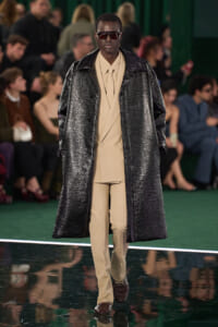 Model walking runway in beige suit with long metallic oversized coat and dark sunglasses