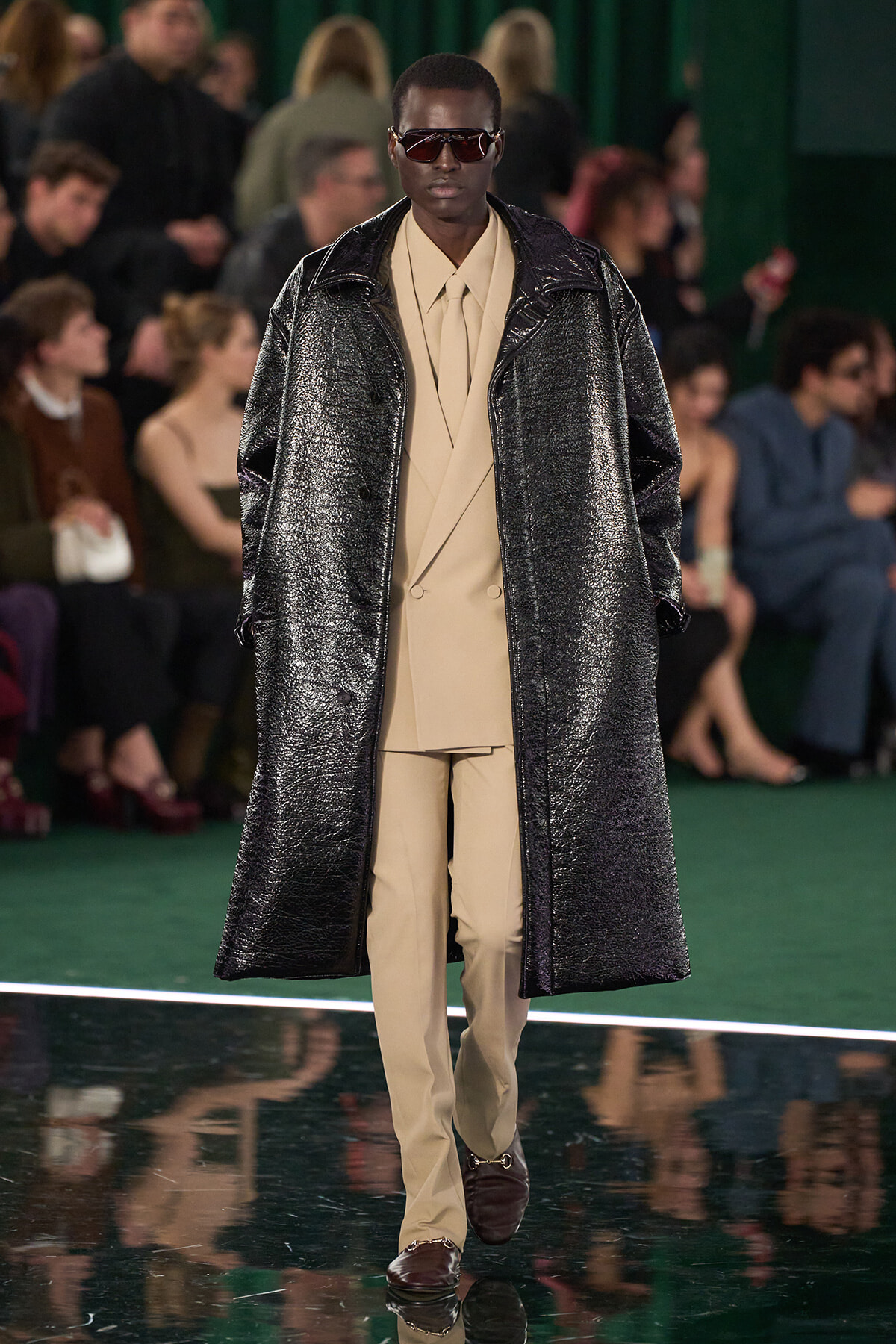 Model walking runway in beige suit with long metallic oversized coat and dark sunglasses