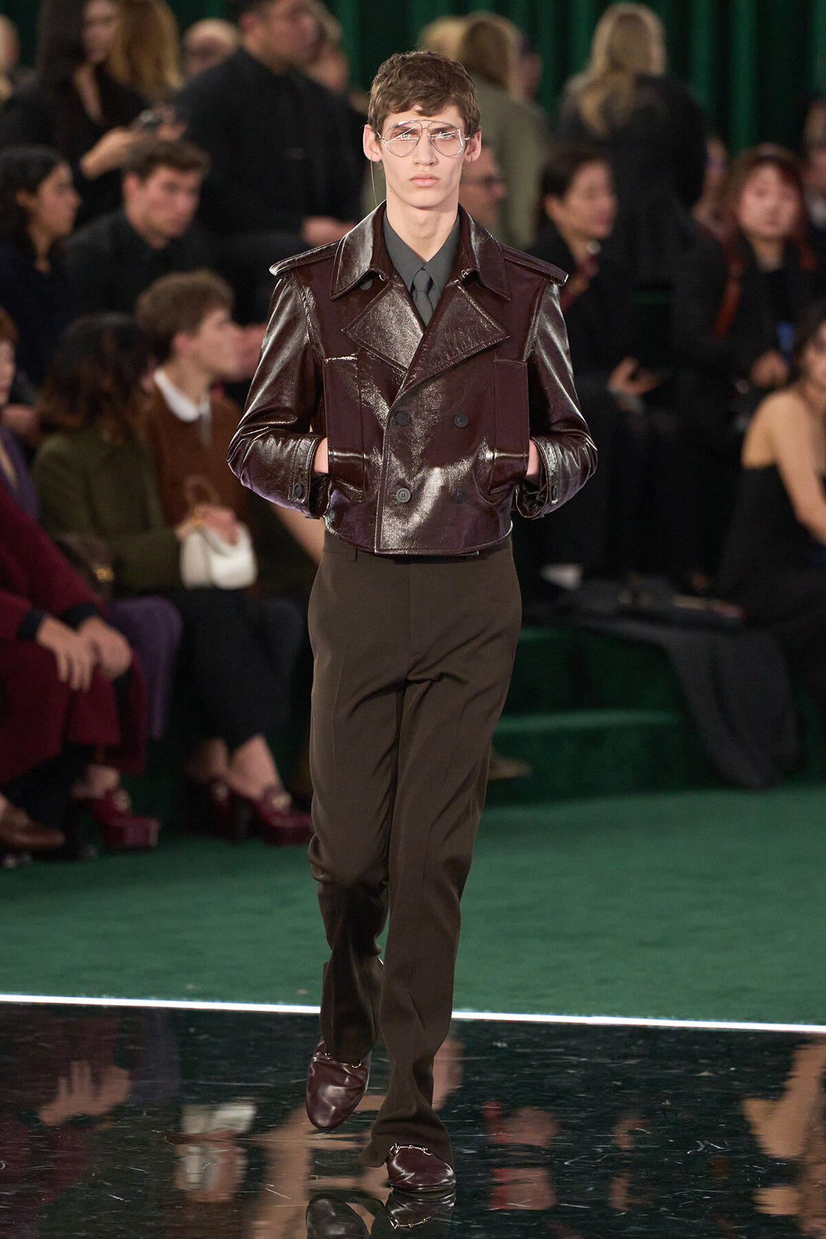 Male model walks the runway in a metallic brown leather double-breasted jacket with matching brown trousers.