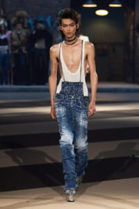 Runway model wearing a white deep-neck tank top with heavily embellished studded denim jeans and glitter platform boots, during a fashion show.