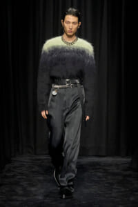 Runway model wearing a gradient fuzzy sweater from light green to black with wide satin gray trousers and a chunky belt.