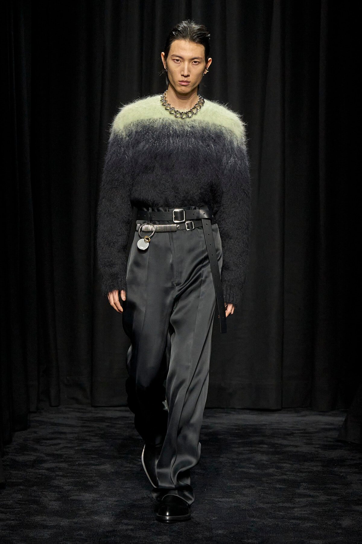 Runway model wearing a gradient fuzzy sweater from light green to black with wide satin gray trousers and a chunky belt.