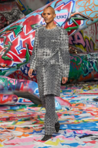 Model wearing a gray textured knit suit walking on a multicolored graffiti-covered runway area.