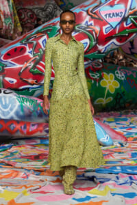 Model in a lime-green sequined long-sleeve top and matching skirt-pants, wearing sunglasses, walking on a graffiti-covered runway.