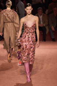 Model walking the runway in a pink, bejeweled slip dress with floral embellishments and matching pink boots.