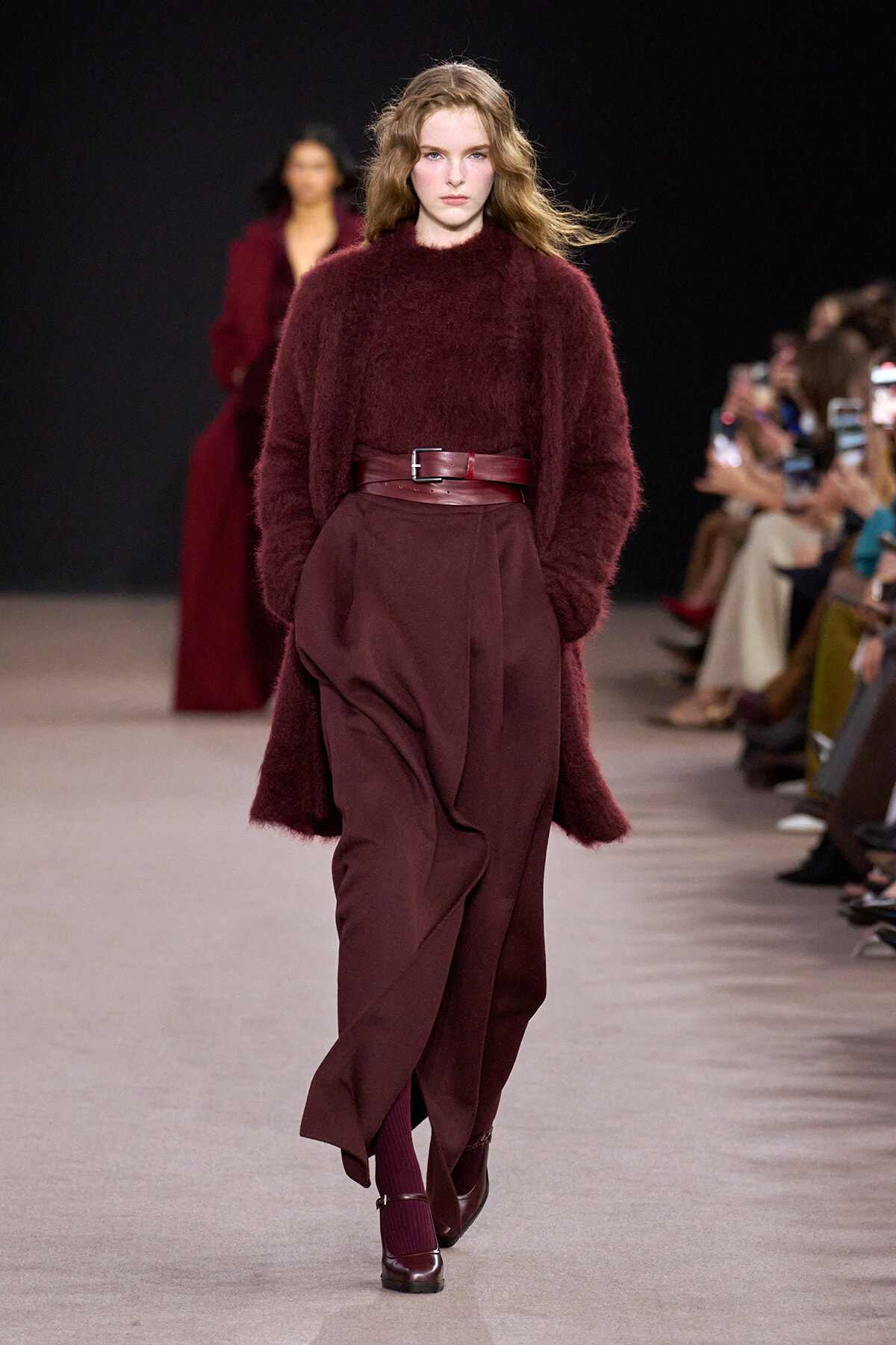 Model walks the runway in a burgundy monochrome outfit: oversized fuzzy burgundy sweater, belted high-waisted wide-leg pants, burgundy shoes, and matching socks.