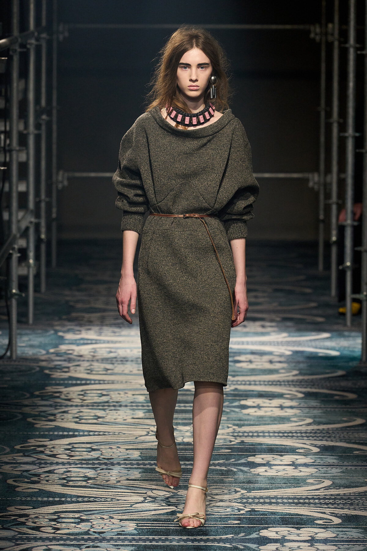 Model walks the runway in a gray knit midi dress belted at the waist, with a chunky pink necklace and beige sandals.