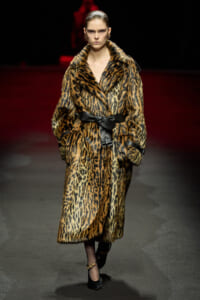 Model walks the runway in a long leopard-print fur coat cinched with a wide black belt and black heels.
