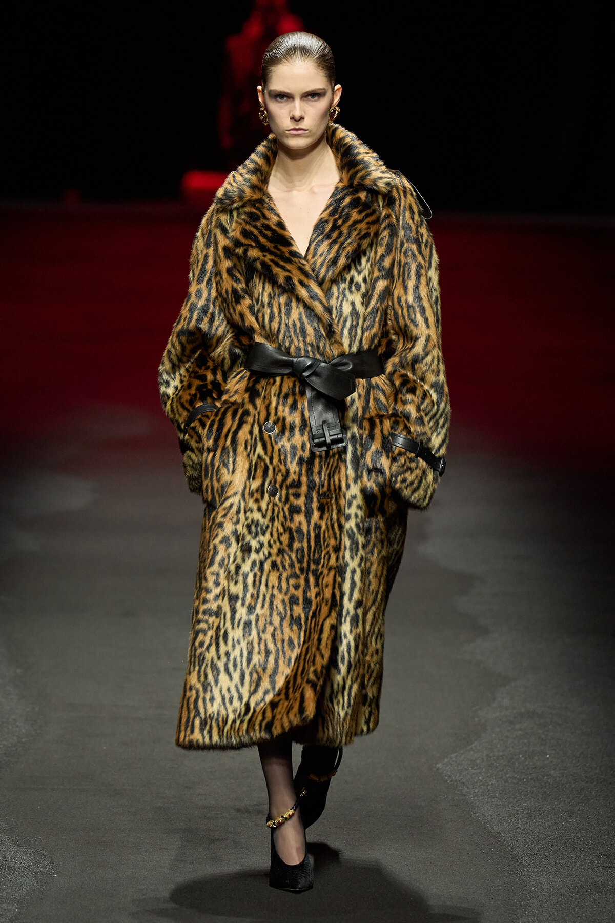 Model walks the runway in a long leopard-print fur coat cinched with a wide black belt and black heels.