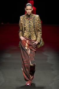 Model on a runway wearing a leopard-print blazer with a matching shirt and wide rust-colored printed pants.