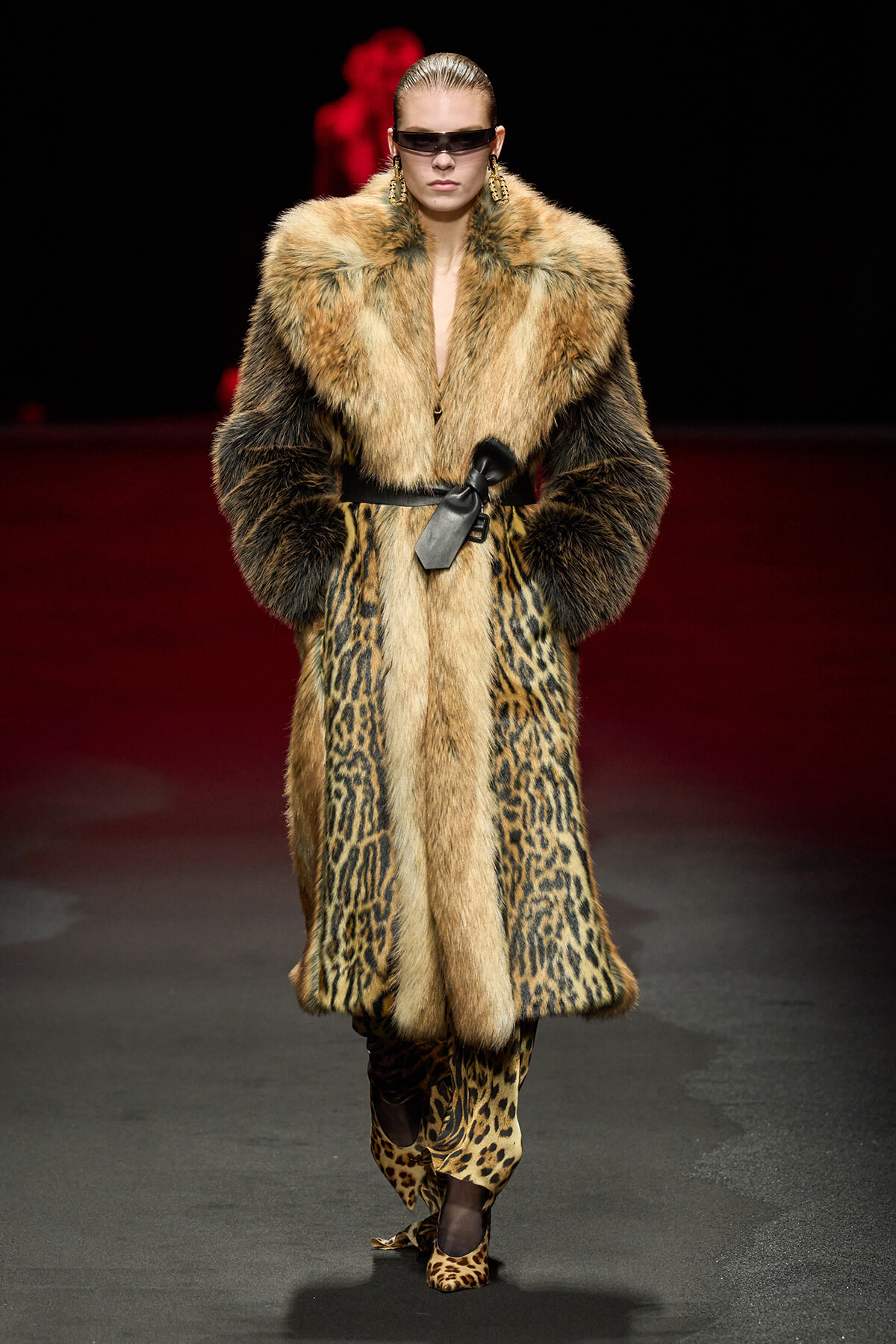 Model struts down a runway in a long leopard-print fur coat with a black belt, oversized sunglasses, and statement earrings.