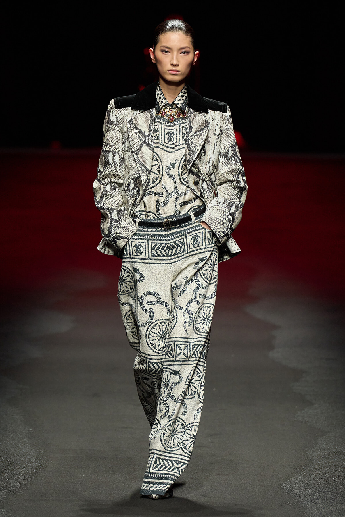 Model walks a fashion runway in a monochrome snakeskin-pattern suit with an oversized jacket and matching trousers.