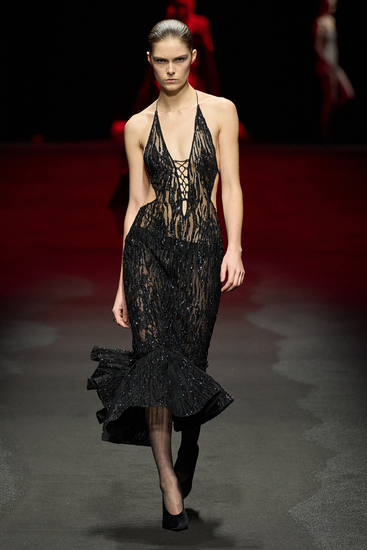 Model walks the runway in a black sequined mermaid gown with a deep V-neck and lace-up front.
