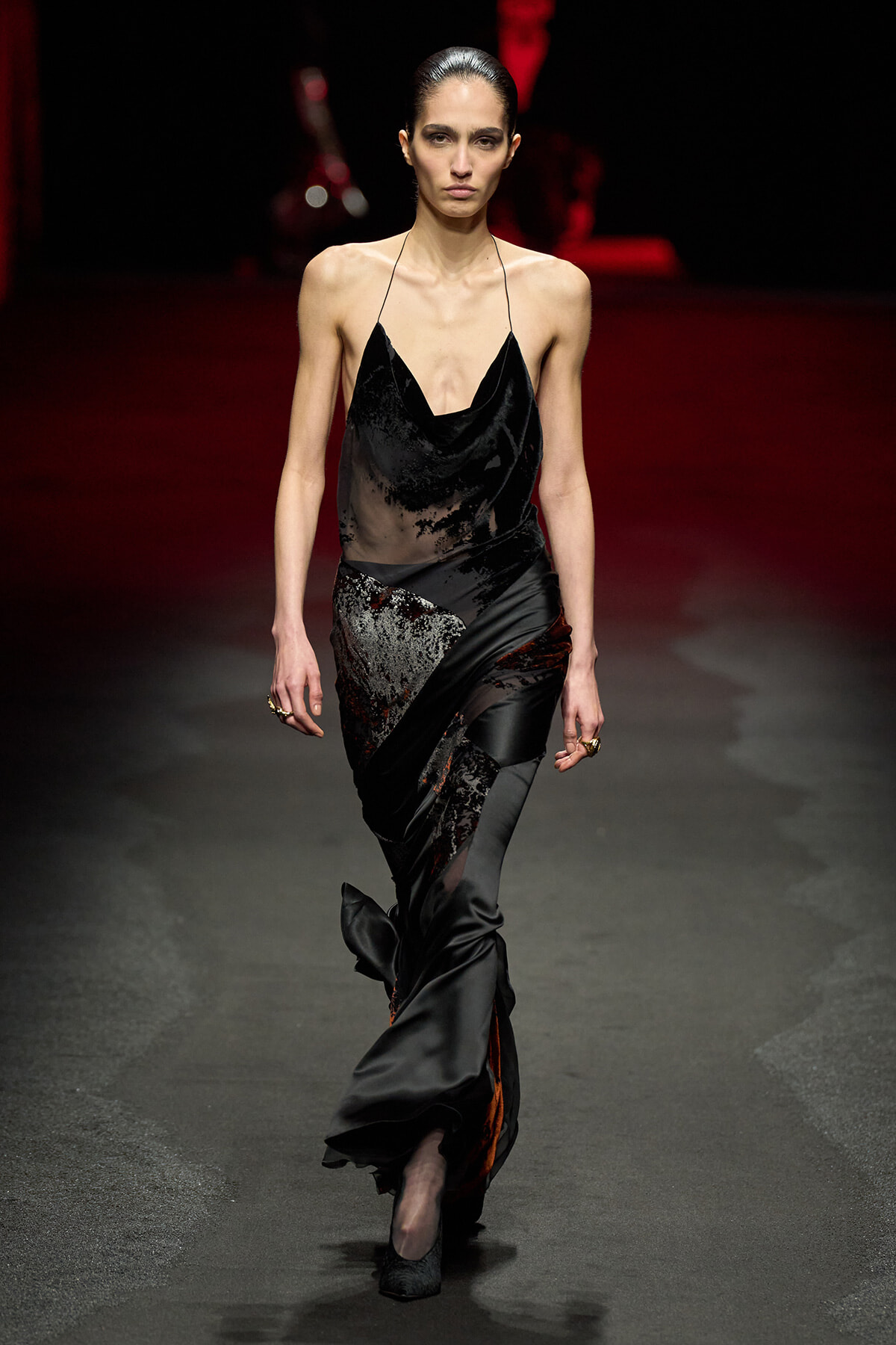 Model walks the runway in a black draped satin slip dress with delicate spaghetti straps and a flowing, sculpted skirt.
