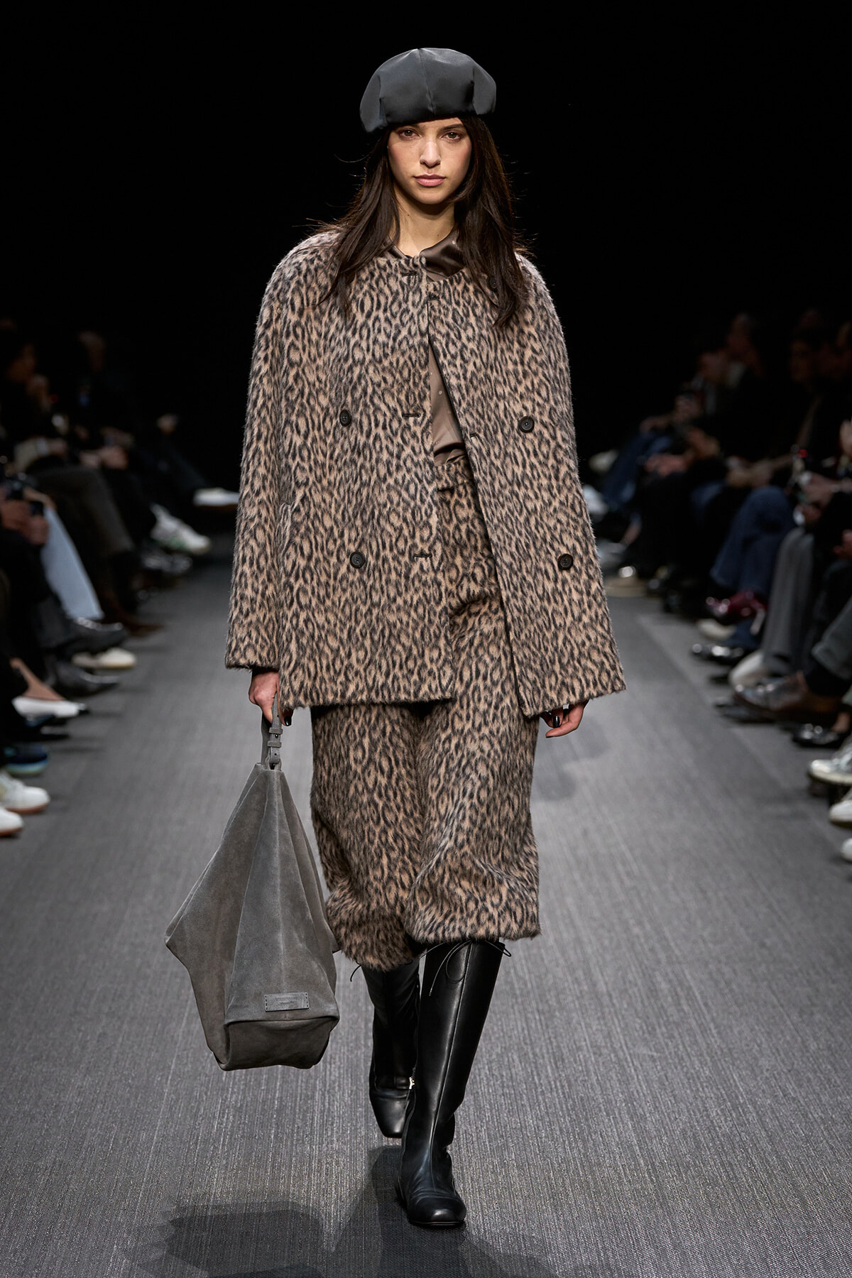 Model walking the runway in a leopard-print coat and matching pants, paired with a gray beret and knee-high black boots, carrying a large gray bag.