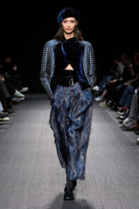 Model walking a runway in a navy velvet jacket with patterned sleeves and wide, watercolor-blue pants; matching velvet beret.