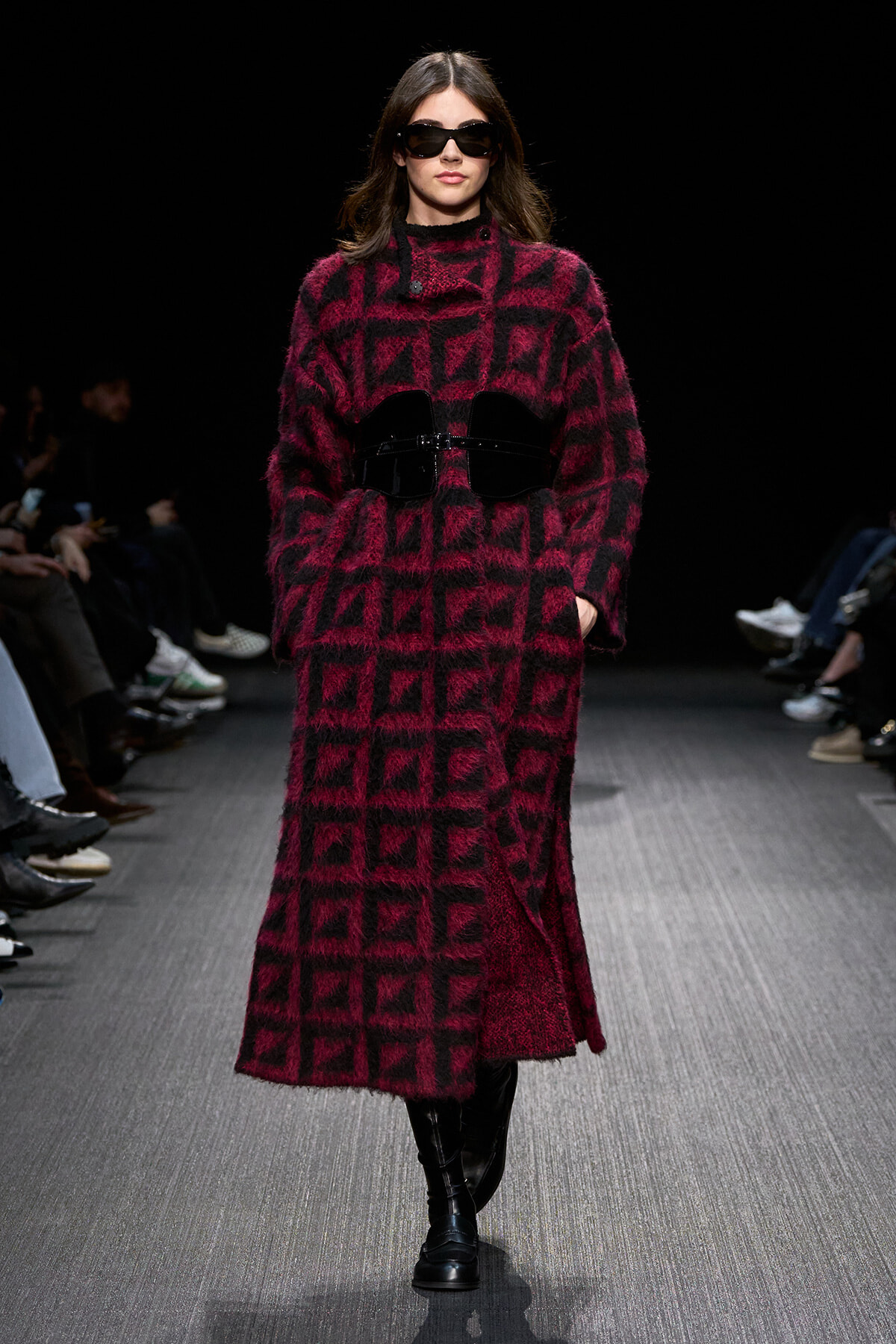 Model walks the runway in a burgundy and black fuzzy geometric coat with a wide black belt and sunglasses,