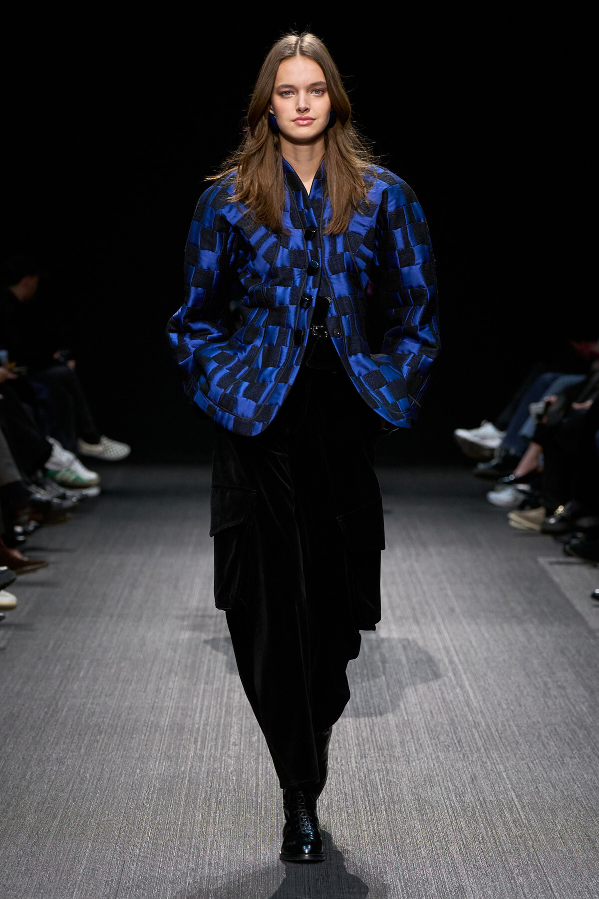 Model walking a runway in a blue checkered quilted jacket and black cargo pants, with black boots.