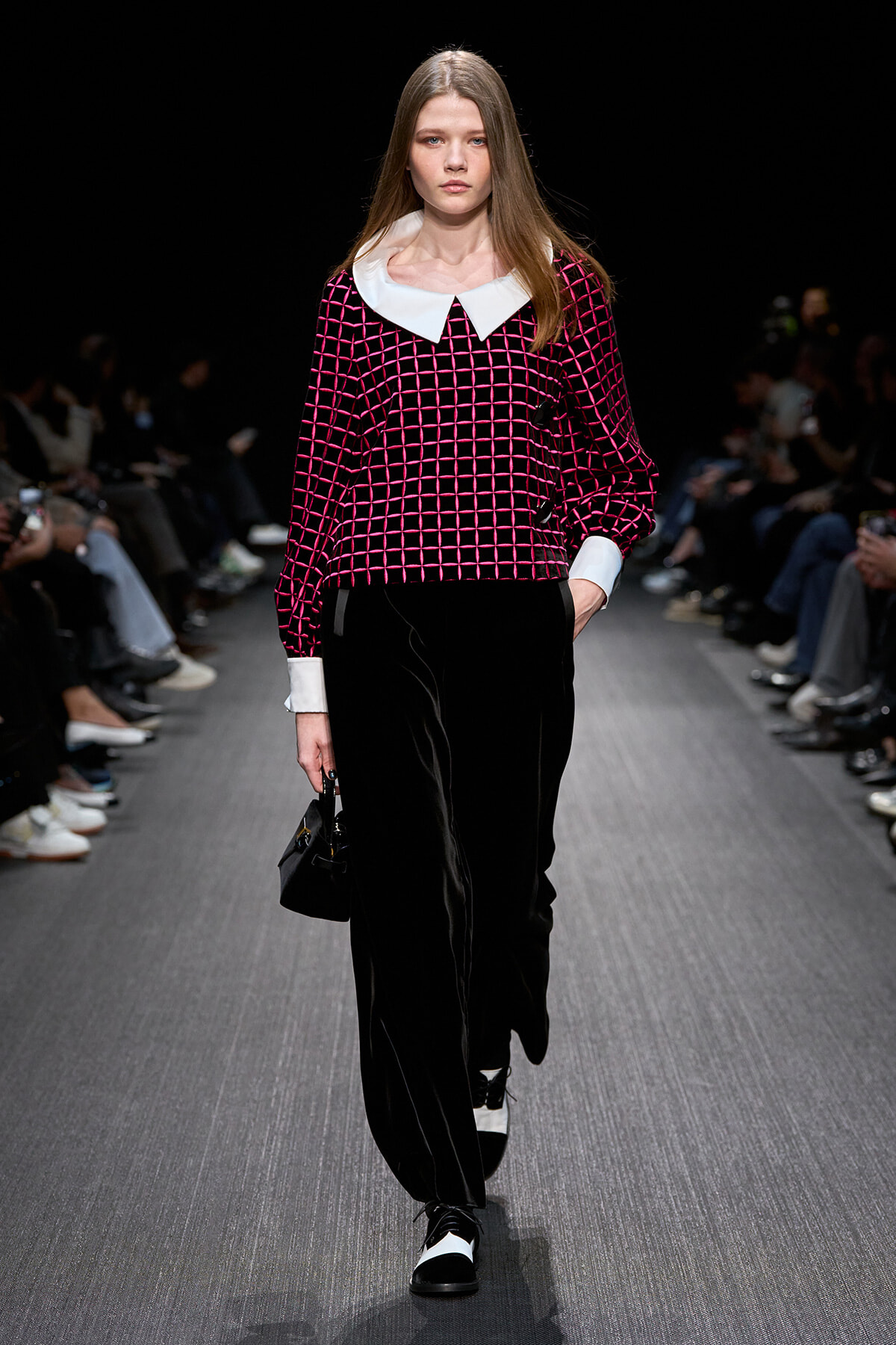 Model walks the runway in a black velvet wide-leg pant suit with a pink grid-pattern top and a white Peter Pan collar; small black handbag in hand.