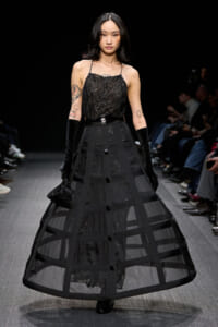 Model walks a fashion runway in a black beaded halter top and voluminous layered mesh skirt with long gloves.