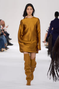 Model walking a runway in a metallic gold satin mini dress with matching tall boots