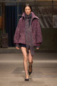 Model walks a fashion runway in an oversized maroon knit coat with matching scarf and pointed heels.