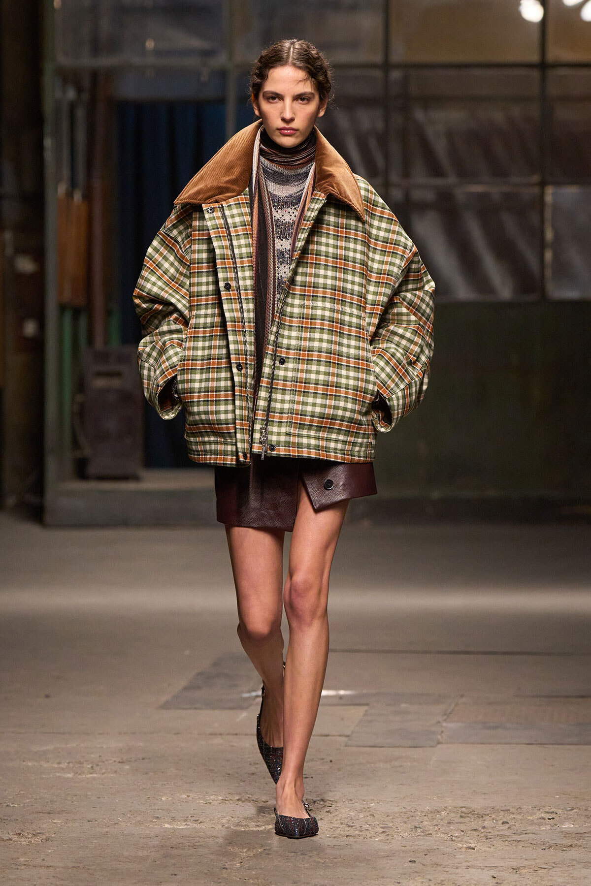 Model walks a runway in an oversized plaid coat with a brown suede collar, layered over a striped turtleneck and burgundy mini skirt, finishing with glittery flats