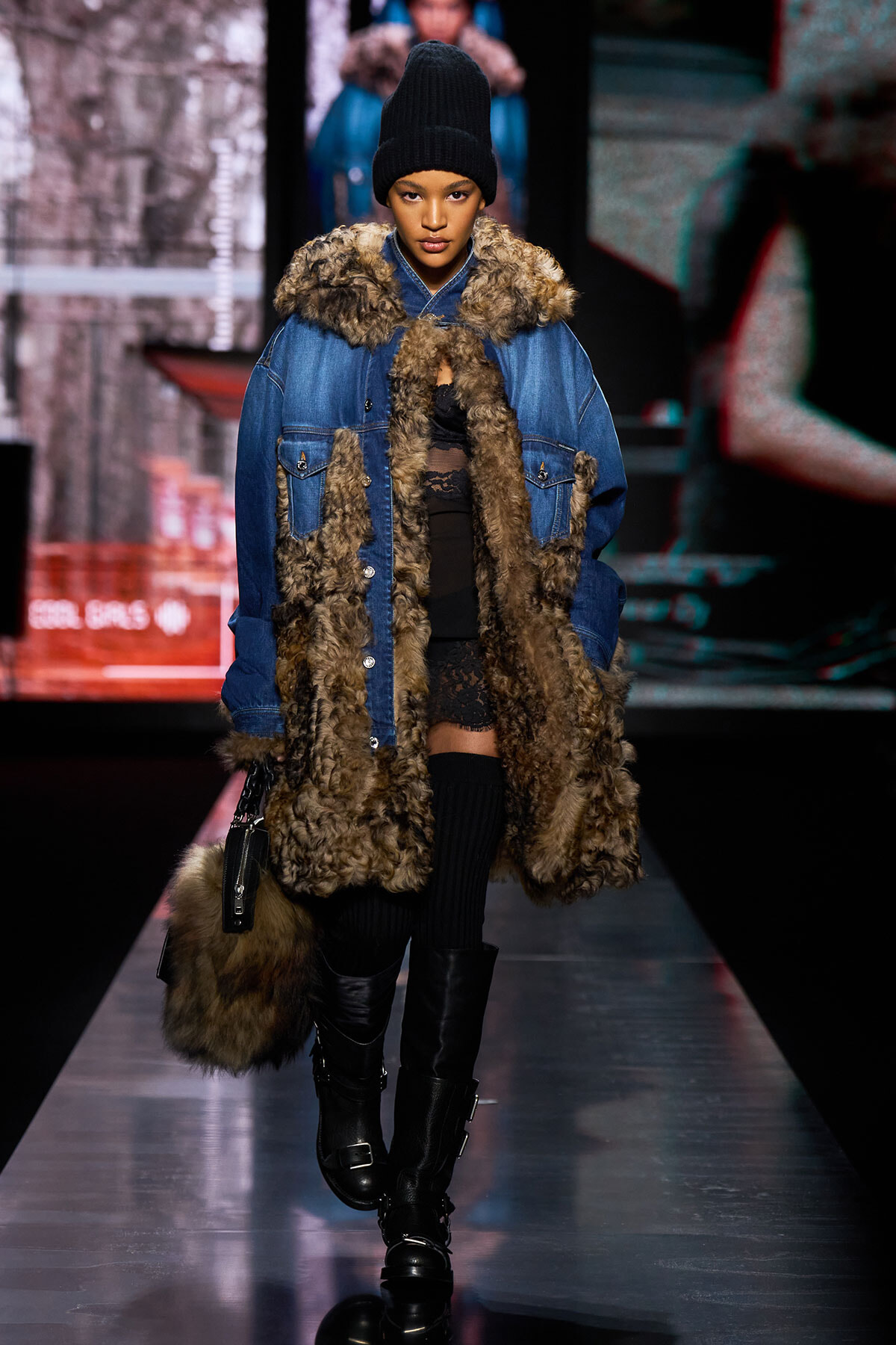 Model walks the runway in an oversized blue denim coat with brown fur trim, black knit beanie, and knee-high boots.