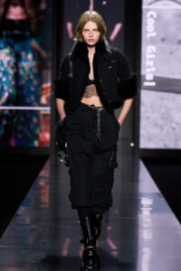 Model walking the runway in a black cropped jacket with fur cuffs, lace top, and loose cargo pants with chunky boots.