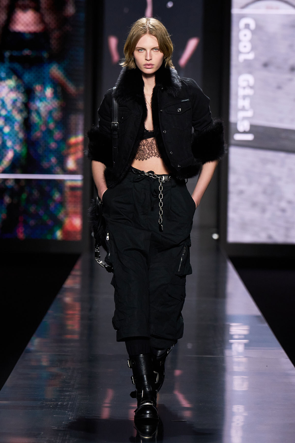 Model walking the runway in a black cropped jacket with fur cuffs, lace top, and loose cargo pants with chunky boots.