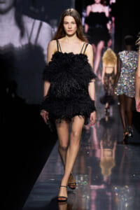 Model walks the runway in a black feathered mini dress with thin straps.