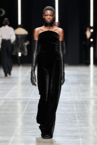 Runway model wearing a black velvet strapless jumpsuit with long matching gloves and a black choker.
