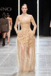 Model walking a nude-toned lace evening gown with sheer overlay on a runway.