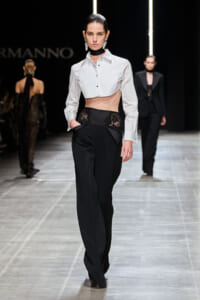 Model walks the runway in a white cropped shirt and black high-waisted pants with a lace waist panel.