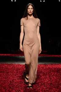 Female model walking a beige jumpsuit on a red petal-covered runway.
