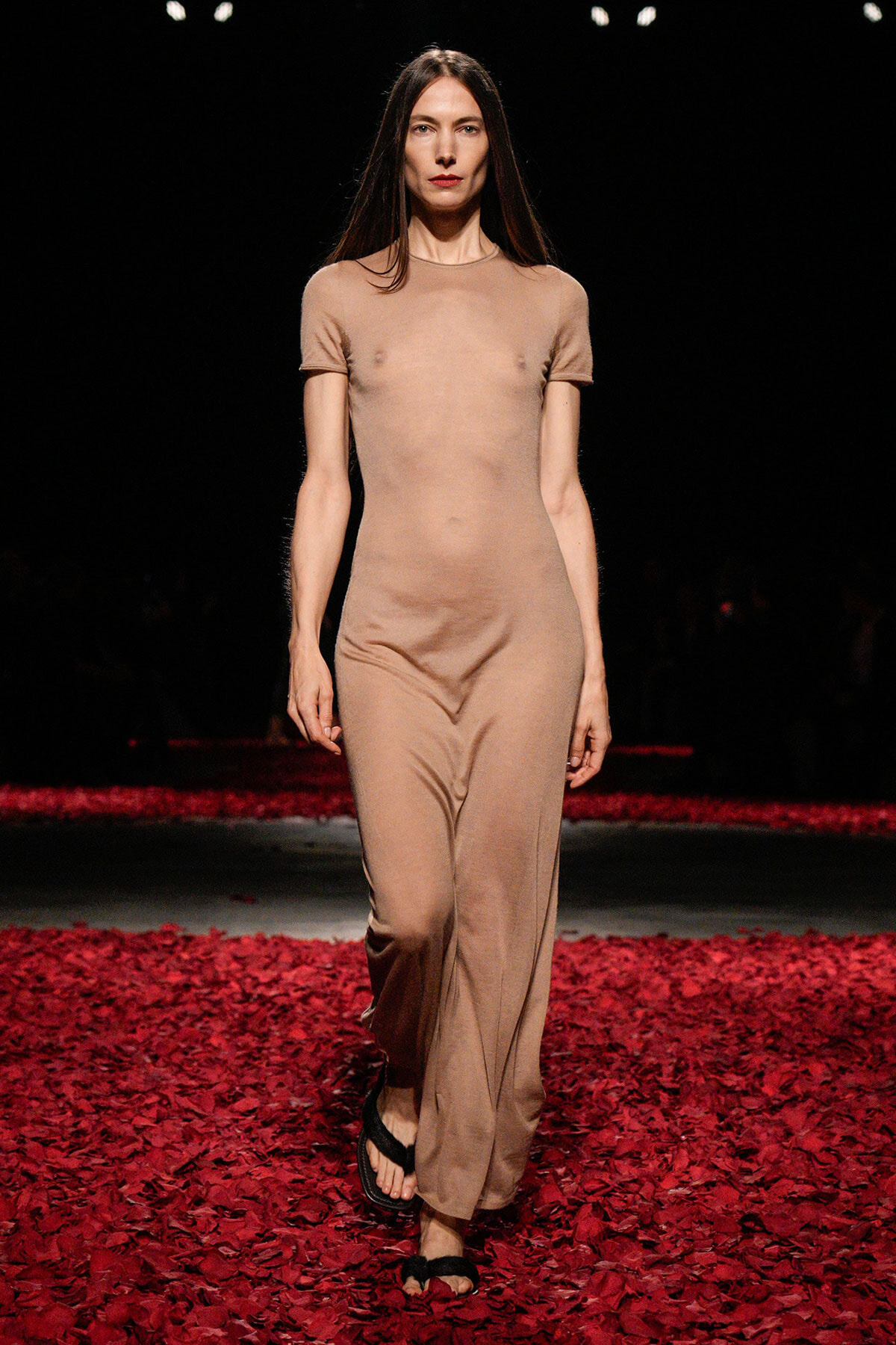 Female model walking a beige jumpsuit on a red petal-covered runway.