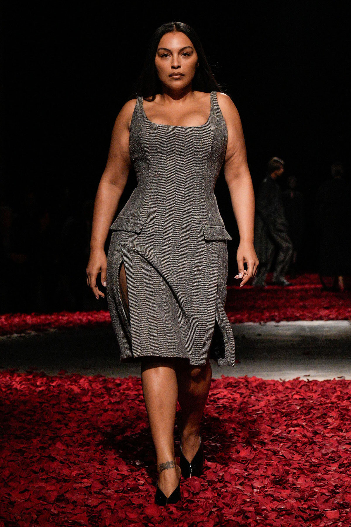 Plus-size model walks the runway in a silver-gray textured dress with side slits, black heels, and red petals on the floor.
