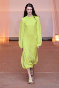 Runway model wearing a neon lime green, long-sleeve sheer dress with a gathered neckline and voluminous bubble hem.