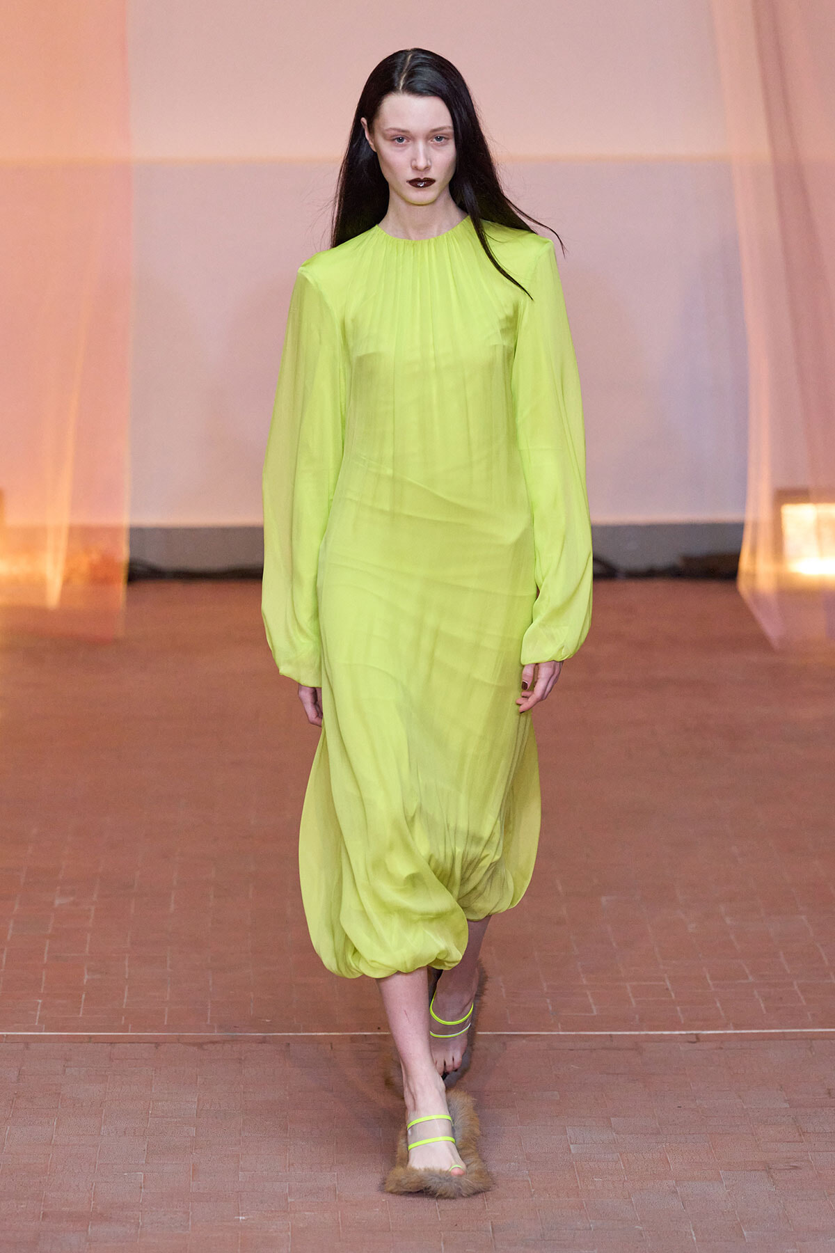 Runway model wearing a neon lime green, long-sleeve sheer dress with a gathered neckline and voluminous bubble hem.