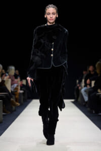 Model walks the runway in a black velvet suit with a patterned velvet scarf and gold buttons.