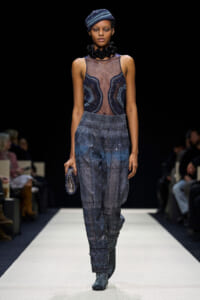 Runway model wearing a blue beaded sheer bodice with sparkling wide-leg pants and a matching blue turban, walking a white runway.